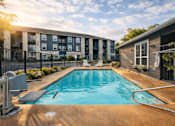 Thumbnail 1 of 25 - A swimming pool in front of a building with a sunny day.