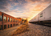 Thumbnail 3 of 9 - A train is passing by a row of buildings.