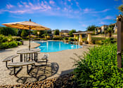 Thumbnail 39 of 61 - A pool area with a table and chairs and a sun umbrella.