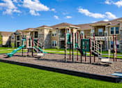 Thumbnail 49 of 61 - A playground with a green slide and a red and green swing set in front of apartment buildings.