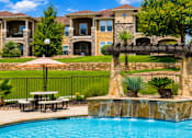 Thumbnail 60 of 61 - A pool with a waterfall and a bench in front of a house.