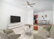 Thumbnail 25 of 25 - A living room with a grey couch, a white TV stand, and a glass coffee table.