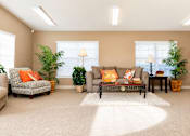 Thumbnail 6 of 8 - A living room with a grey couch, a chair, a coffee table, and two potted plants.