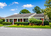Thumbnail 2 of 8 - A house with a red brick facade and a grey roof is surrounded by greenery and a clear blue sky.