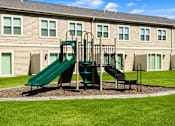 Thumbnail 18 of 19 - A playground with a green slide and a black slide in front of a building.