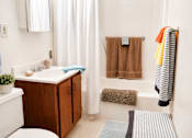 Thumbnail 5 of 8 - A bathroom with a white tub, a wooden cabinet, and a striped towel hanging on the rack.
