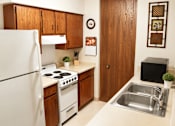 Thumbnail 3 of 8 - A kitchen with a white refrigerator, wooden cabinets, a stove, and a sink.