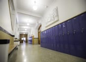 Thumbnail 18 of 39 - A long hallway with purple lockers and a white wall with a drawing on it.