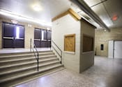 Thumbnail 31 of 39 - A staircase with a black railing leads to a door in a room with a concrete wall.