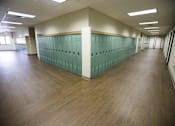 Thumbnail 34 of 39 - A long hallway with green lockers and wood floors.