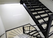 Thumbnail 36 of 39 - A staircase with a black metal railing and a beige carpeted stair.