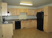 Thumbnail 9 of 12 - A kitchen with tan cabinets and a black refrigerator.