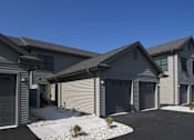 Thumbnail 1 of 12 - A house with a grey garage door and a brown roof.
