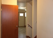 Thumbnail 10 of 17 - A hallway with a brown door on the left and a white door in the distance.
