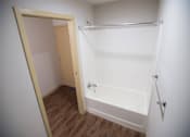 Thumbnail 19 of 21 - A white bathroom with a wooden door and a white bathtub.