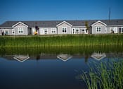 Thumbnail 4 of 21 - A row of houses are reflected in the water in front of them.