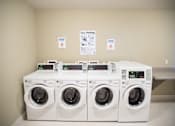 Thumbnail 11 of 13 - A row of white washing machines are in a room with instructions on the wall.