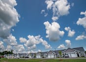 Thumbnail 13 of 13 - A row of houses with a blue sky and fluffy white clouds above.