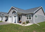Thumbnail 1 of 13 - A grey house with a white garage door and windows.