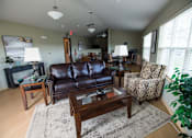 Thumbnail 6 of 13 - A living room with a brown leather couch, a patterned chair, and a coffee table.