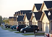Thumbnail 5 of 15 - A street view of a residential area with cars parked on the side of the road and houses with triangular roofs.