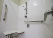 Thumbnail 21 of 21 - A white shower stall with a white bench and a silver grab bar.