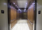 Thumbnail 12 of 27 - A long hallway with wood panels and elevator doors on either side.