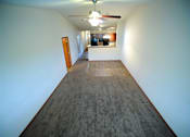 Thumbnail 9 of 13 - A long hallway with a carpeted floor and a ceiling fan.