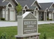 Thumbnail 6 of 13 - A sign for Mission Village of Sheboygan stands in front of a building.