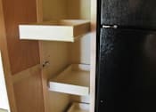 Thumbnail 9 of 18 - A black refrigerator is next to a wooden cabinet with two shelves.