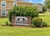 Thumbnail 9 of 11 - A sign for Wood Valley Apartments is in the foreground of a grassy area.