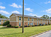 Thumbnail 7 of 11 - A long brick building with a brown roof and a sign on the front.