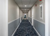 Thumbnail 4 of 25 - A long hallway with a carpeted floor and white walls.