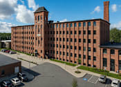 Thumbnail 18 of 18 - A large red brick building with a tower and a parking lot in front.