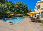 Thumbnail 27 of 27 - A pool area with a bench and chairs under umbrellas.