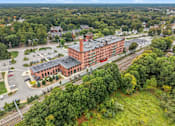 Thumbnail 28 of 29 - A large red brick building is surrounded by trees and a parking lot.