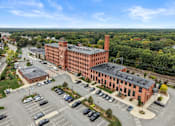 Thumbnail 27 of 29 - A large red brick building with a parking lot in front.