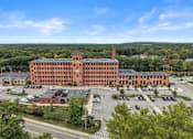 Thumbnail 26 of 29 - A large red brick building with a parking lot in front.