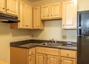 Thumbnail 6 of 12 - A kitchen with wooden cabinets and a black refrigerator.