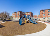Thumbnail 12 of 17 - A playground with a blue slide in front of a brick building.