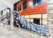 Thumbnail 11 of 17 - A large mural of a hand is displayed on a brick wall in a spacious room.