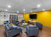 Thumbnail 10 of 14 - A living room with a grey sofa, a grey armchair, a coffee table, a bookshelf, and a TV. at Ship's Watch Apartments, Fall River, MA, 02720