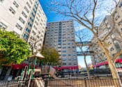 Thumbnail 3 of 8 - A playground with a slide and a tree in front of apartment buildings.