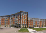 Thumbnail 4 of 12 - A large brick building with a curved top floor and a parking lot in front. at The Anne M. Lynch Homes at Old Colony, South Boston, Massachusetts