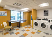 Thumbnail 12 of 15 - Community laundry center with washers and seating at Baystate Place Apartments, Massachusetts