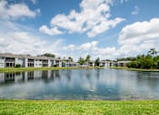 Thumbnail 14 of 14 - A serene lake in front of a row of houses under a blue sky with clouds Fishermans Landing Apartments in Ormond Beach, FL.
