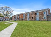 Thumbnail 9 of 21 - A building with a stone facade and a green lawn in front.