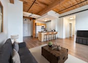 Thumbnail 1 of 15 - A living room with a grey couch and a wooden coffee table at The Cordovan at Haverhill Station, Haverhill, MA
