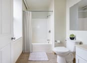 Thumbnail 4 of 15 - A white bathroom with a toilet, sink, and bathtub at The Cordovan at Haverhill Station, Haverhill, MA