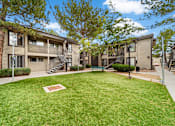 Thumbnail 19 of 20 - A grassy area in front of apartment buildings with a bench and a tree.